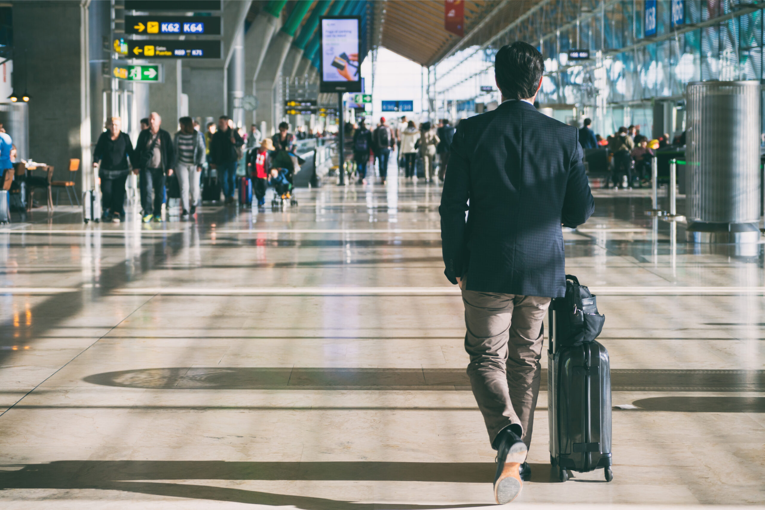 Close up of businessman carrying suitcase while walking through a passenger departure terminal in airport.